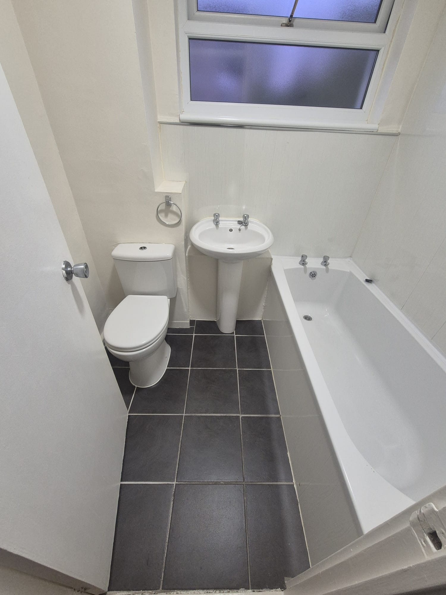 Old white bathroom with pedestal basin, dated WC and grey floor tiles before renovation